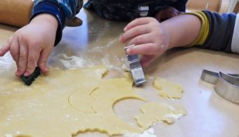 Zu sehen sind die Hände von zwei Kindern. Sie halten Ausstecher und sind gerade dabei Plätzchen aus dem Teig auszustechen. 