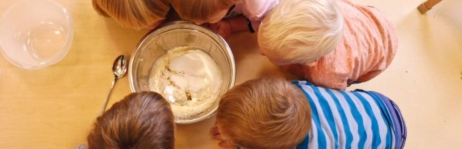 Zu sehen sind die Köpfe von mehreren Kindern, wie sie in eine Schüssel mit Backzutaten schauen.