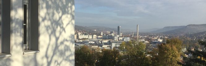 Auf der linken Seite des Bildes sieht man etwas vom Gebäude der Kita. Der Blick geht ins Tal. Dort sieht man den Jentower Turm und die Innenstadt im Sonnenlicht.